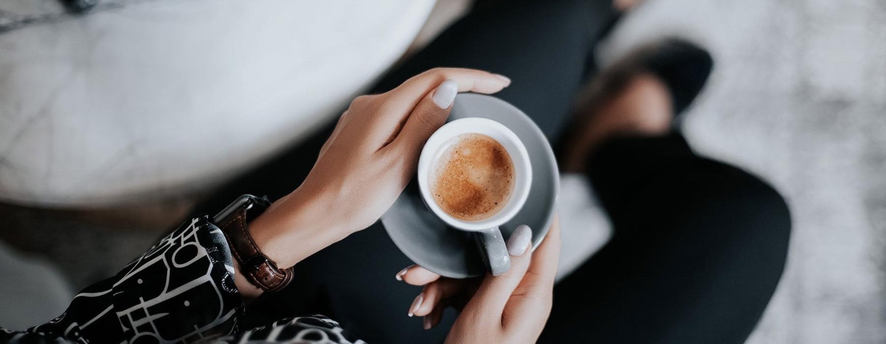 business woman sits next to a marble table with books and holds a saucer with a cup of espresso